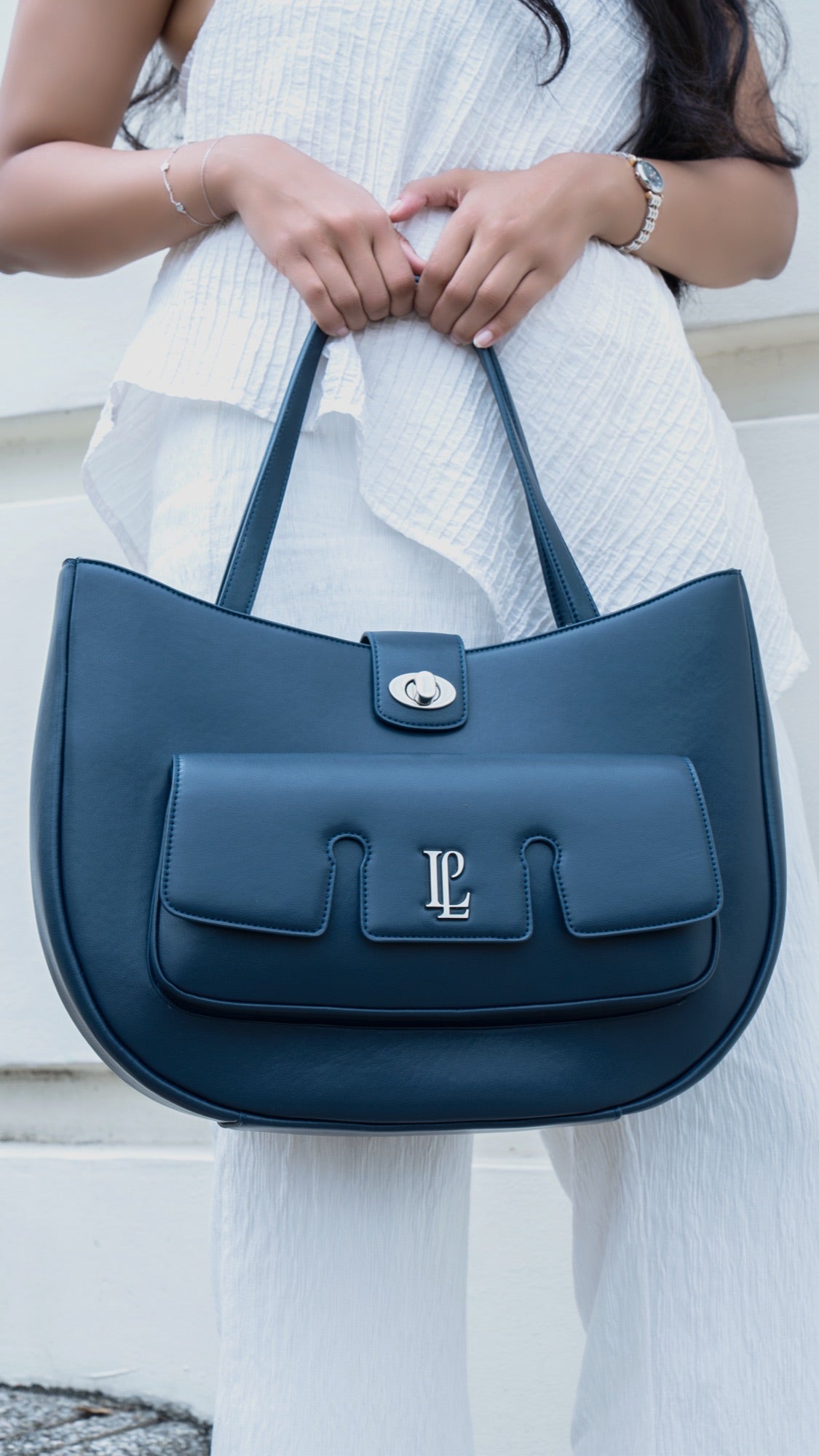 The Levain bag in Flint grey carried by a model in a floral summer dress, walking through a garden